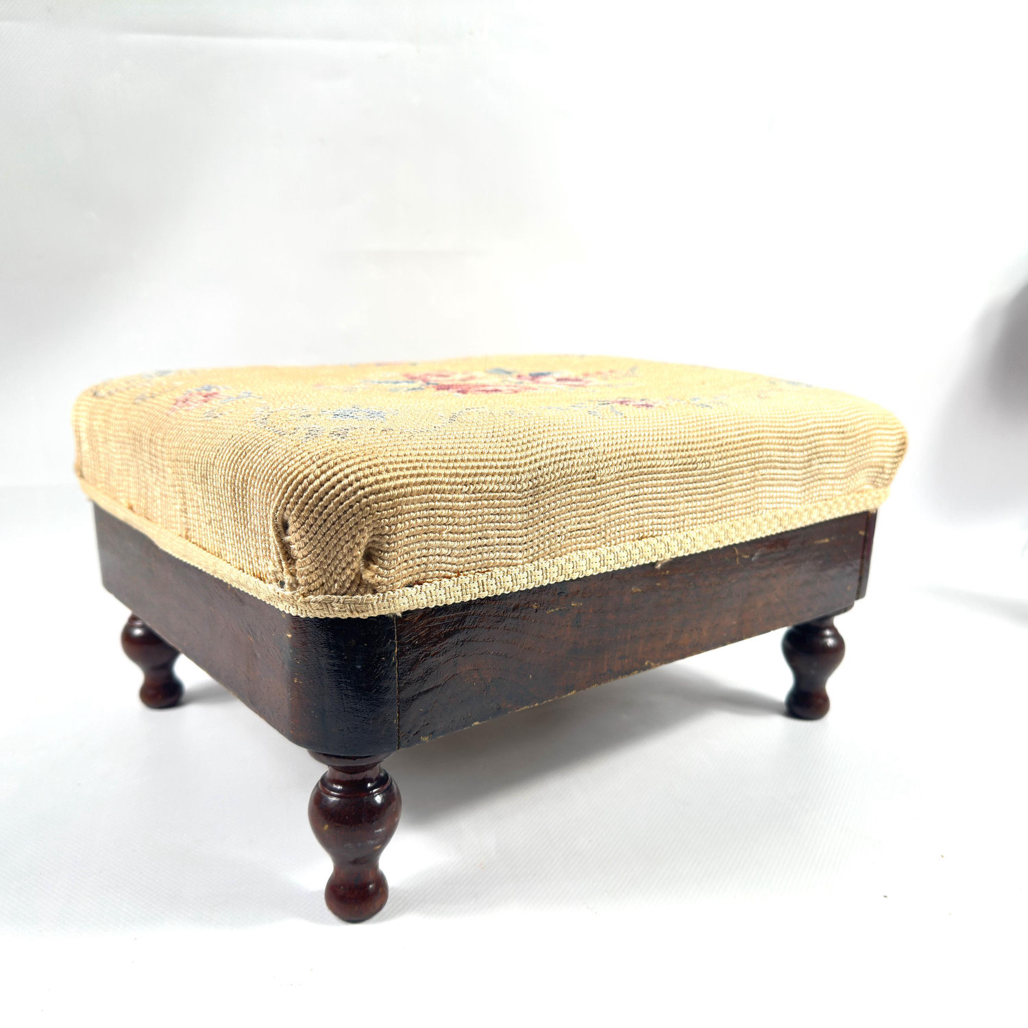 Three-quarter view of cream tapestry footstool displaying rounded wooden legs and structured silhouette