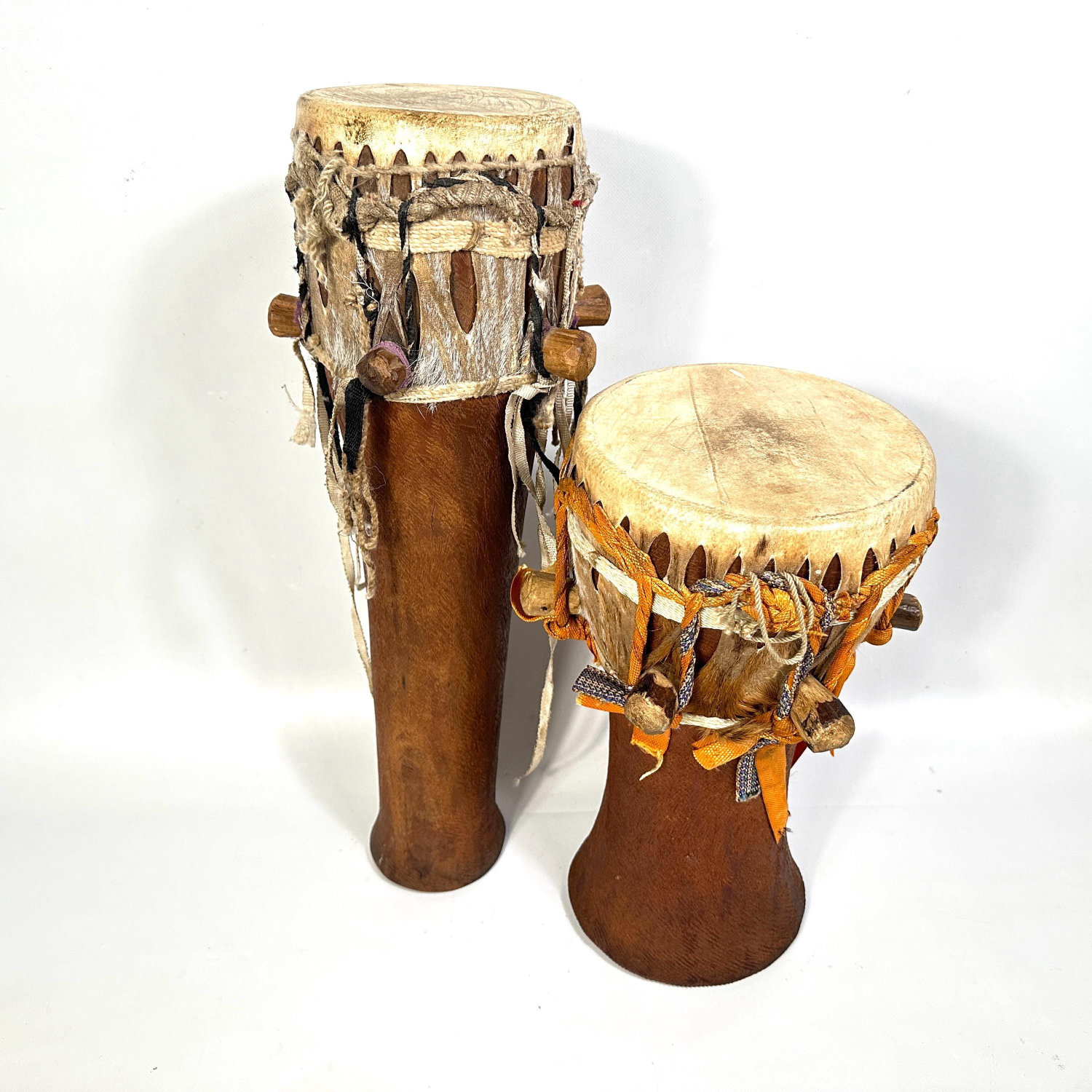Two larger African hand drums with natural hide heads and visible carved wooden bodies showing rope tensioning detail