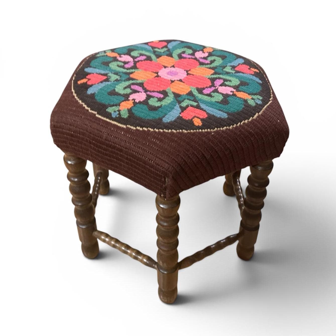 Vintage footstool full view, centered composition, chocolate brown needlepoint fabric, floral embroidered design, five turned
