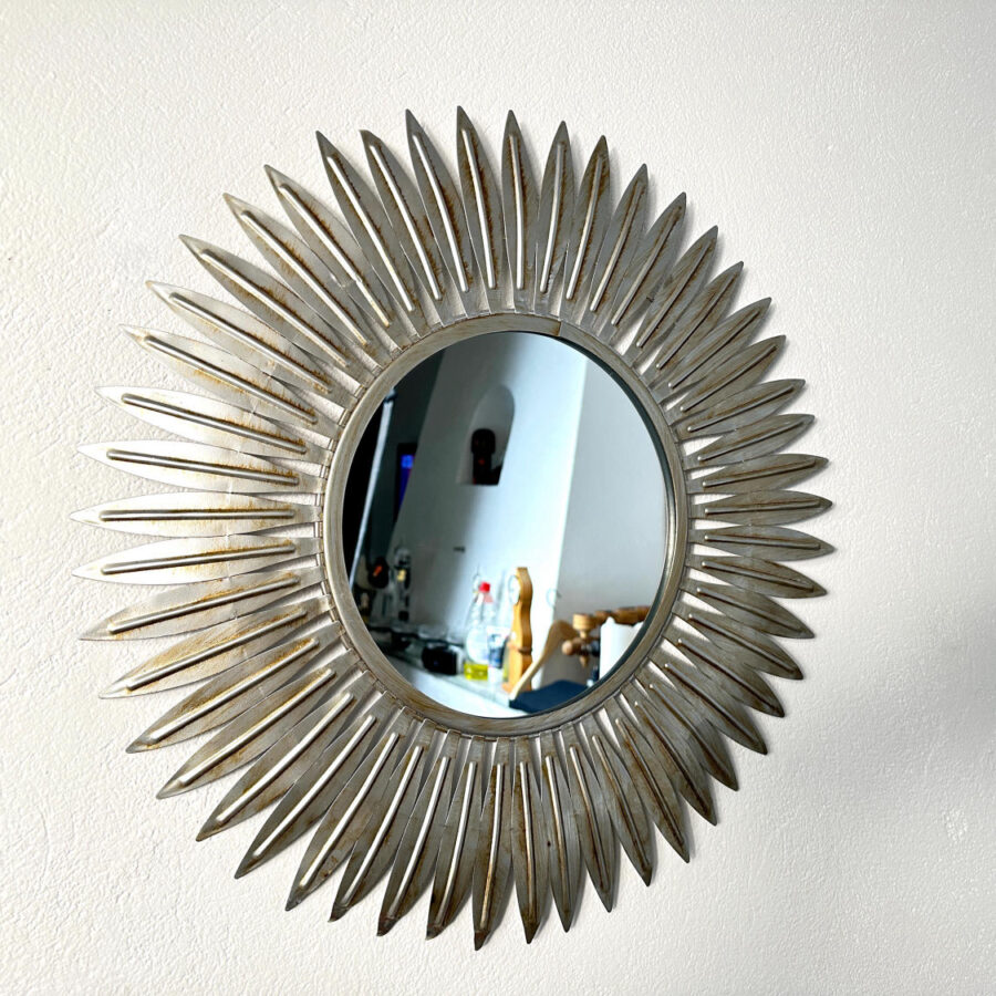 Silver sunburst mirror with radiating leaf-form frame, antiqued metallic finish, mid-century Hollywood Regency style wall dec