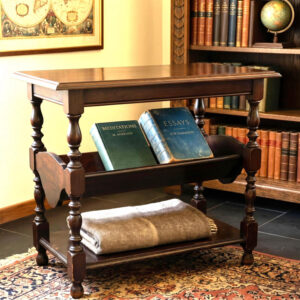 Dark wood Shaker-style side table with turned legs, book rack shelf, and lower storage tier in period room setting