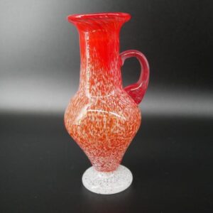 Orrefors hand-blown red glass miniature jug with white speckled base, full front view showing vibrant color gradient and curv