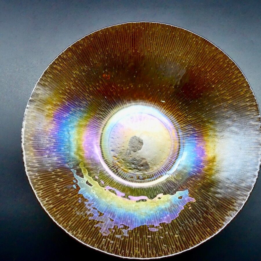 The luminous heart of this piece: rainbow iridescence catches light in endless colors across warm amber tones. Mid-century Scandinavian iridescent glass bowl with marigold orange hues and rainbow luster, top view