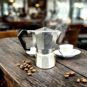 Vintage Junior Express 3-cup aluminum moka pot with black handle, surrounded by coffee beans on wooden surface