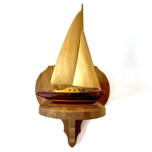 Wooden sailboat with natural sails mounted on carved wall shelf, front-facing nautical display