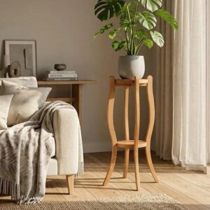 Tall wooden plant stand with curved legs in warm honey oak, styled in modern living room with cream sofa and potted plant