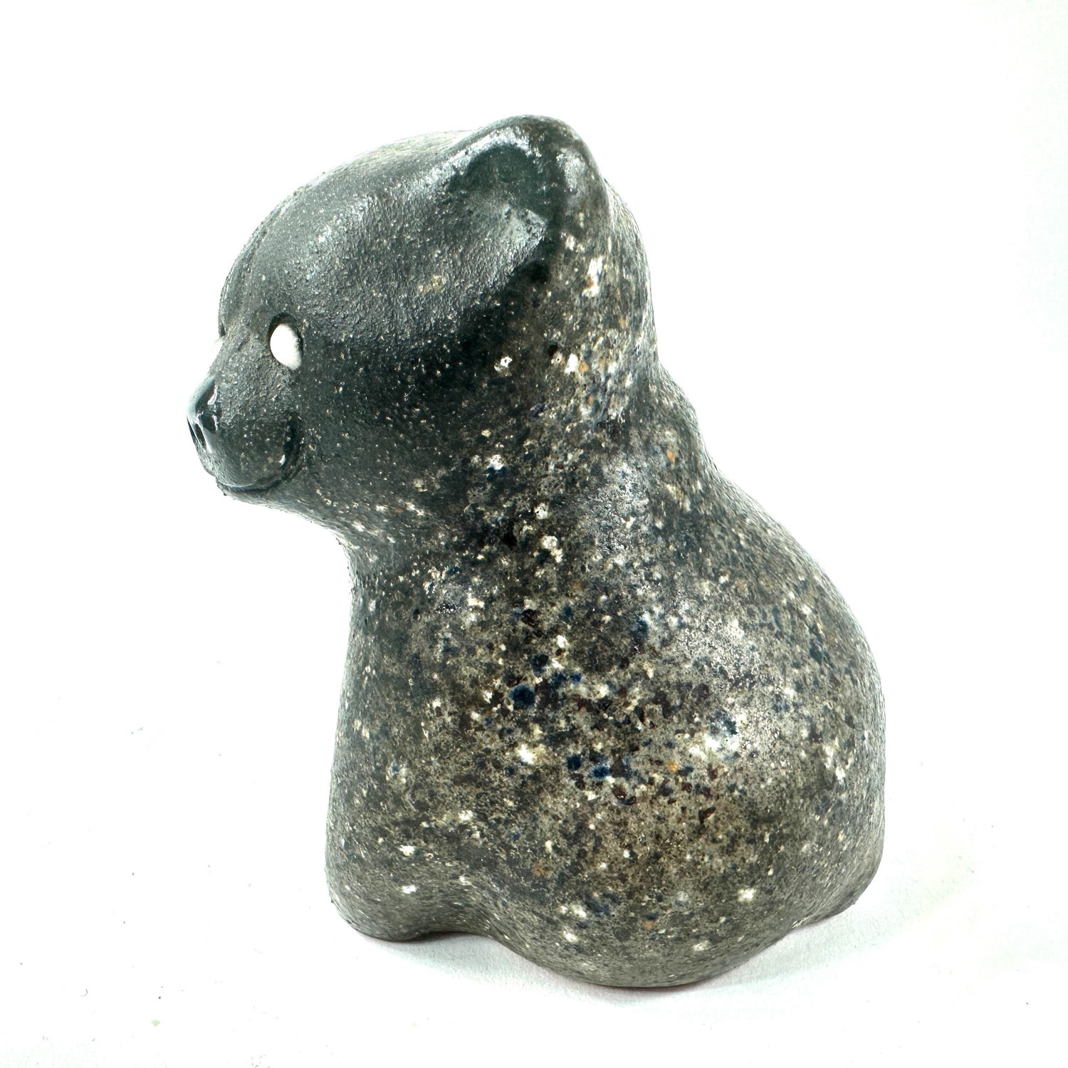 Ceramic bear figurine in profile showing curved back, shoulders, and subtle green-tinted paw painting against neutral backgro