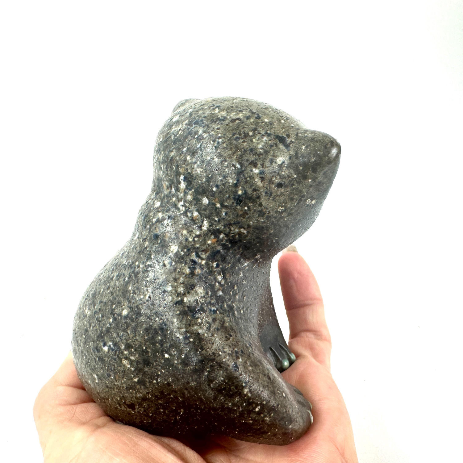 Ceramic bear from behind in hand showing rounded back form, surface texture, and paw articulation in side-rear angle