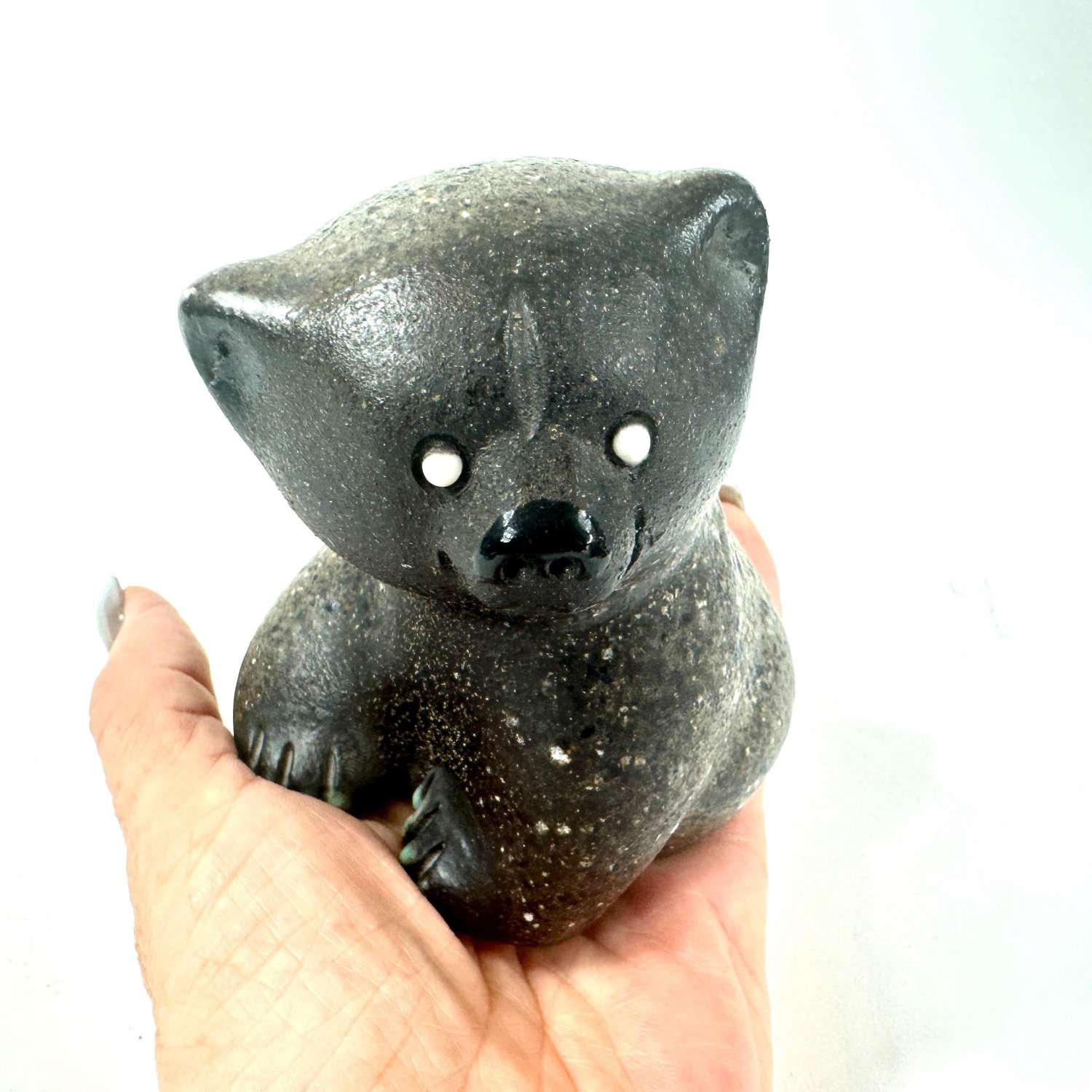 Ceramic bear held in hand showing front face, white inset eyes, black nose, speckled glaze, and intimate scale for collectors