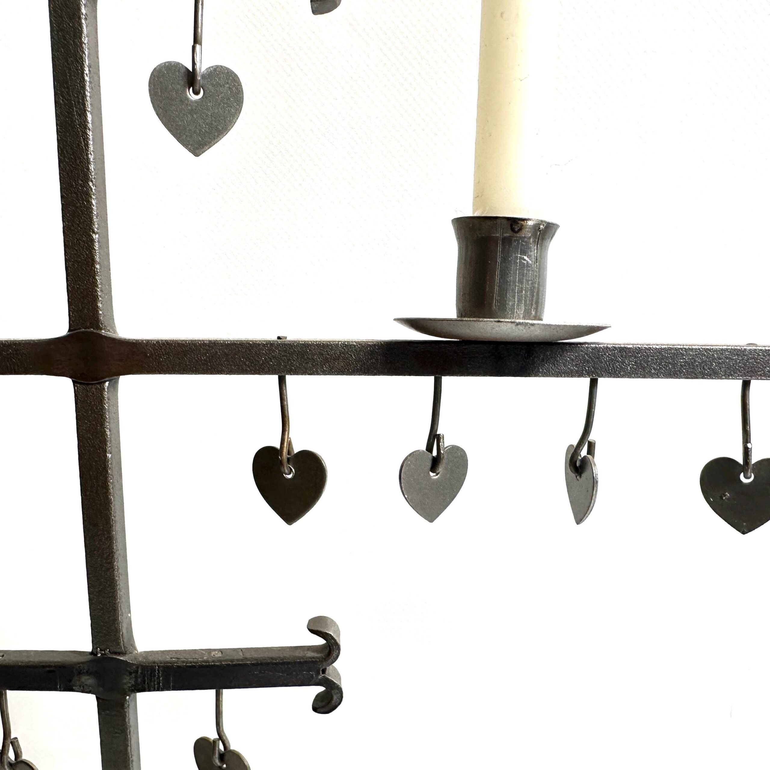 Close-up detail of wrought iron cross arms with suspended heart charms in varying finishes, candle holder visible, textural w