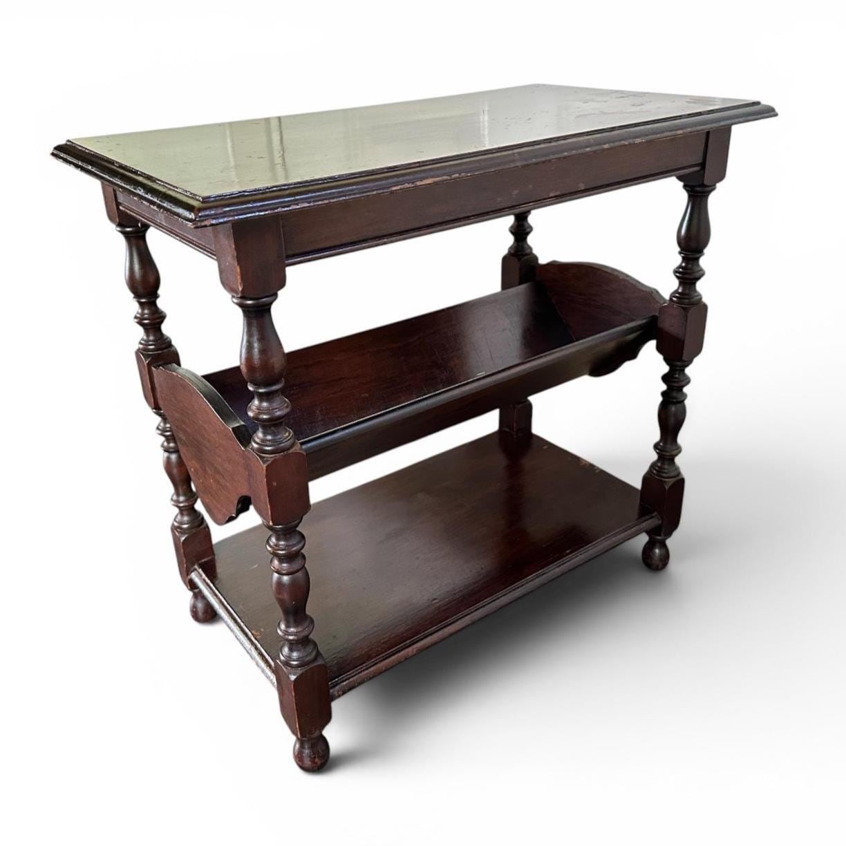 Dark stained wood side table with integrated book trough and dual open storage tiers, clean studio view