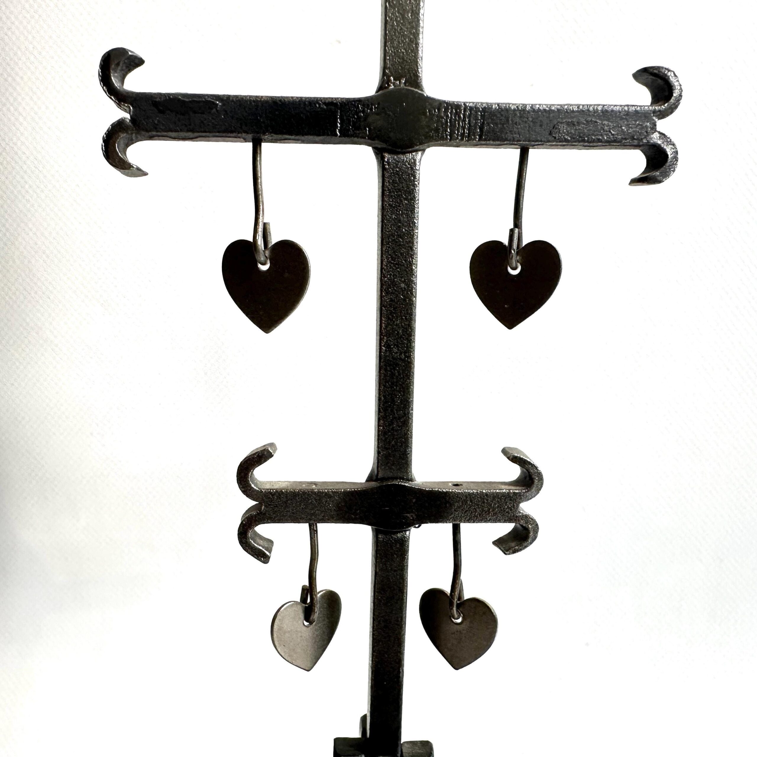 Detailed view of lower tiered iron crossbars displaying contrasting heart pendants in dark iron and silver-toned finishes, sc
