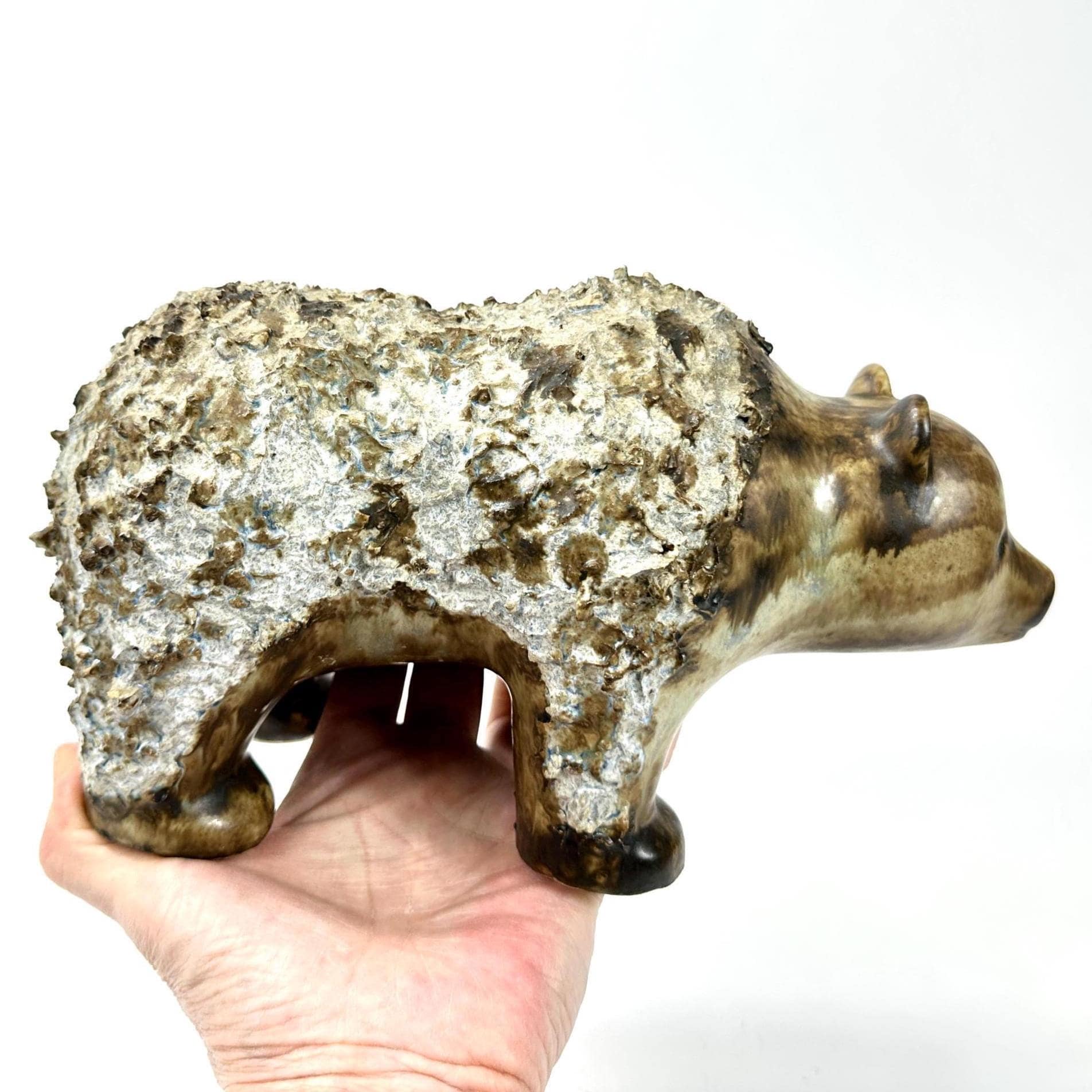 EGO Stengods Swedish stoneware bear sculpture from 1970s, held in hand, showing weathered white-crusted texture and warm brow