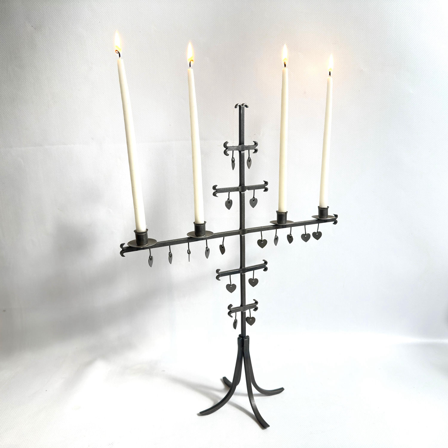 Full-length Ystad-Metall candelabra with four cream candles glowing, heart charms visible across tiered levels, warmly lit st