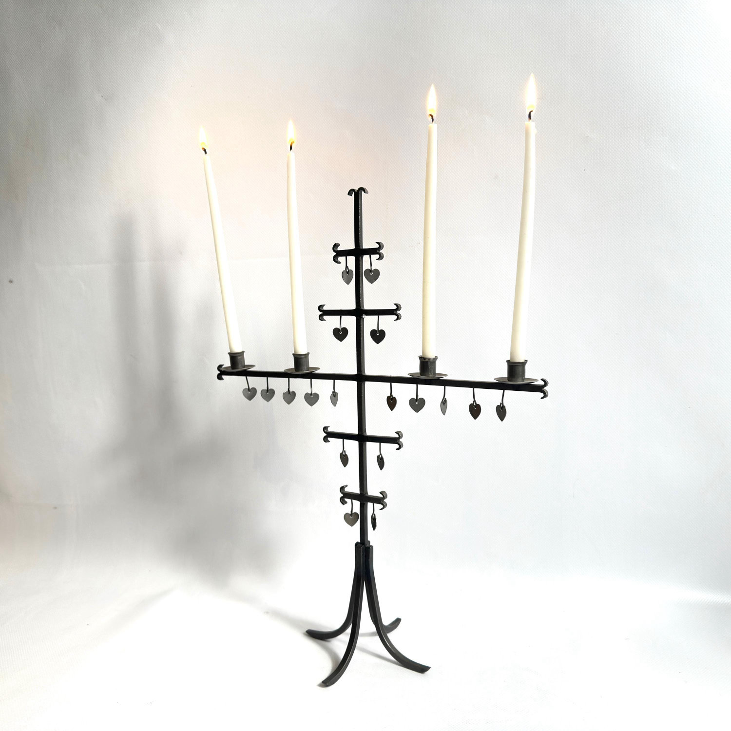 Gunnar Ander candelabra frontal view with four tapers lit, tiered pendant hearts suspended, architectural iron framework clea