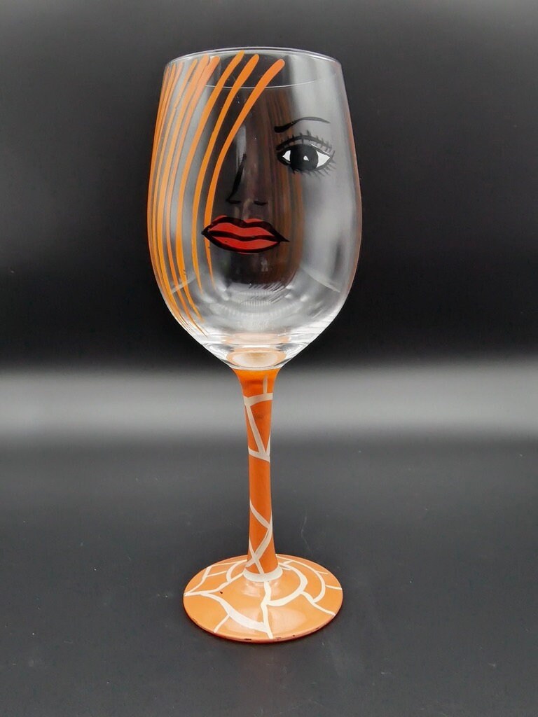 Hand-painted wine glass featuring abstract face with orange striped hair, red lips, and stem on matching base