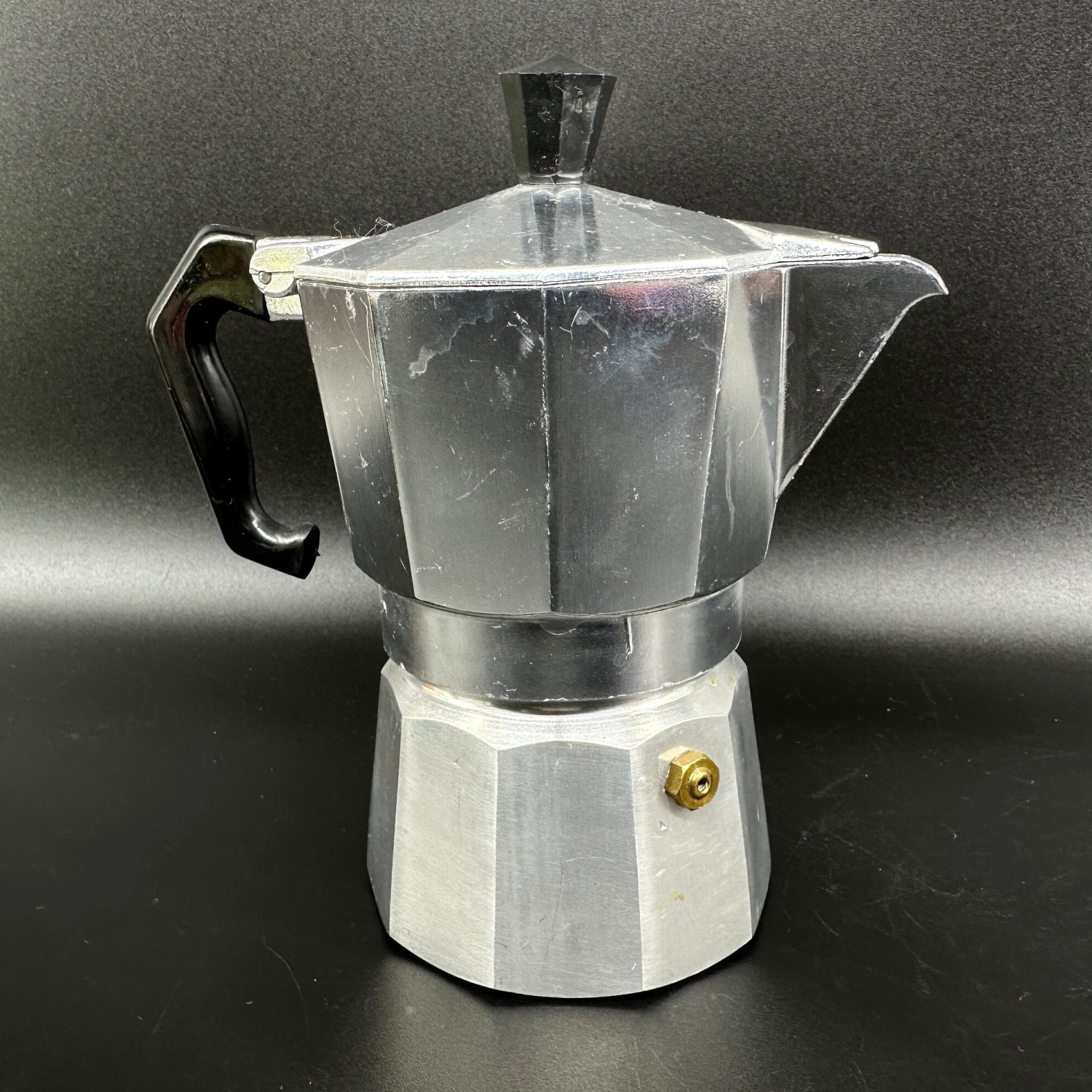Moka pot showing brass safety valve detail on lower chamber with black handle and aluminum construction