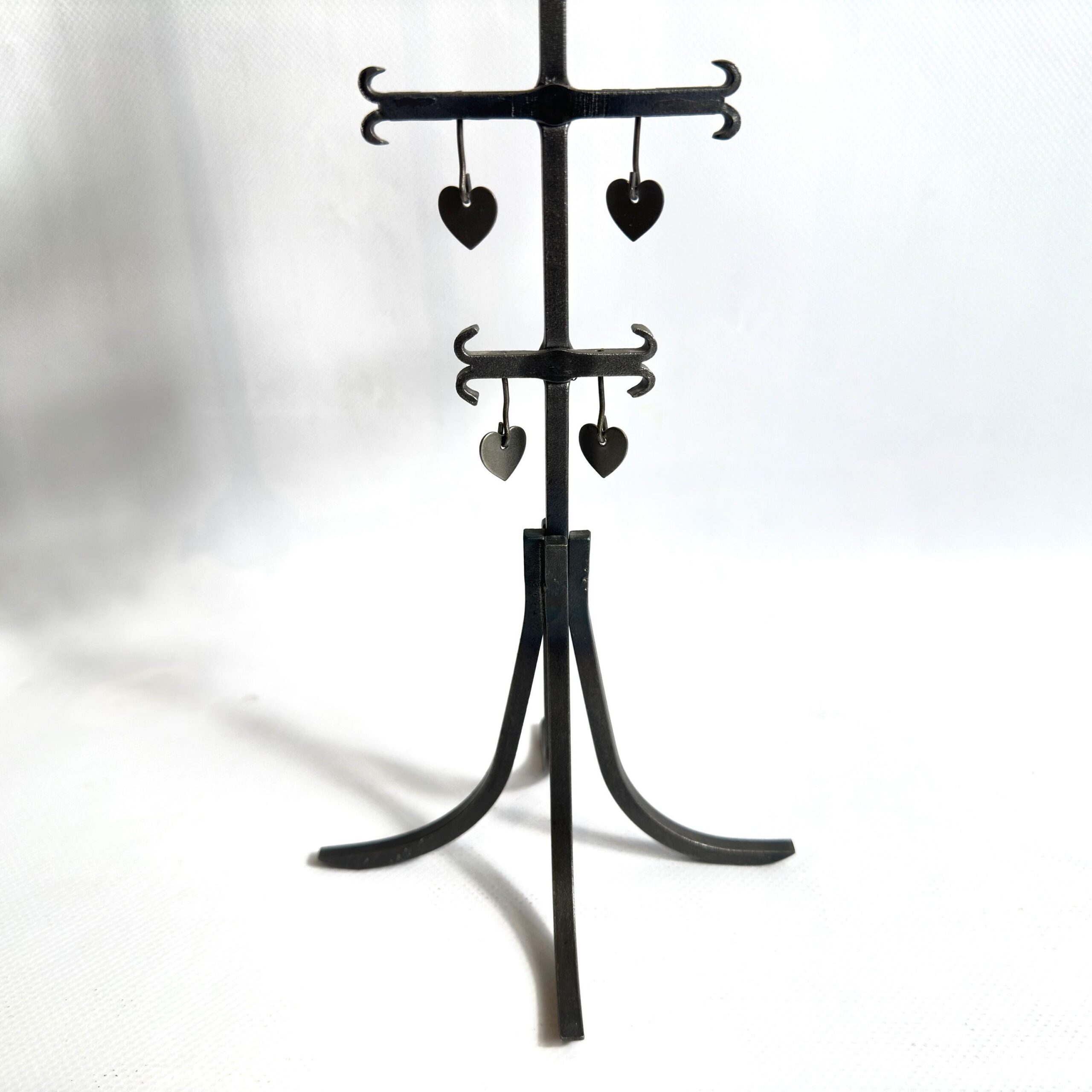 Overhead detail of wrought iron candelabra base with tripod feet and lower tiered crossbars with hanging heart pendants, clos