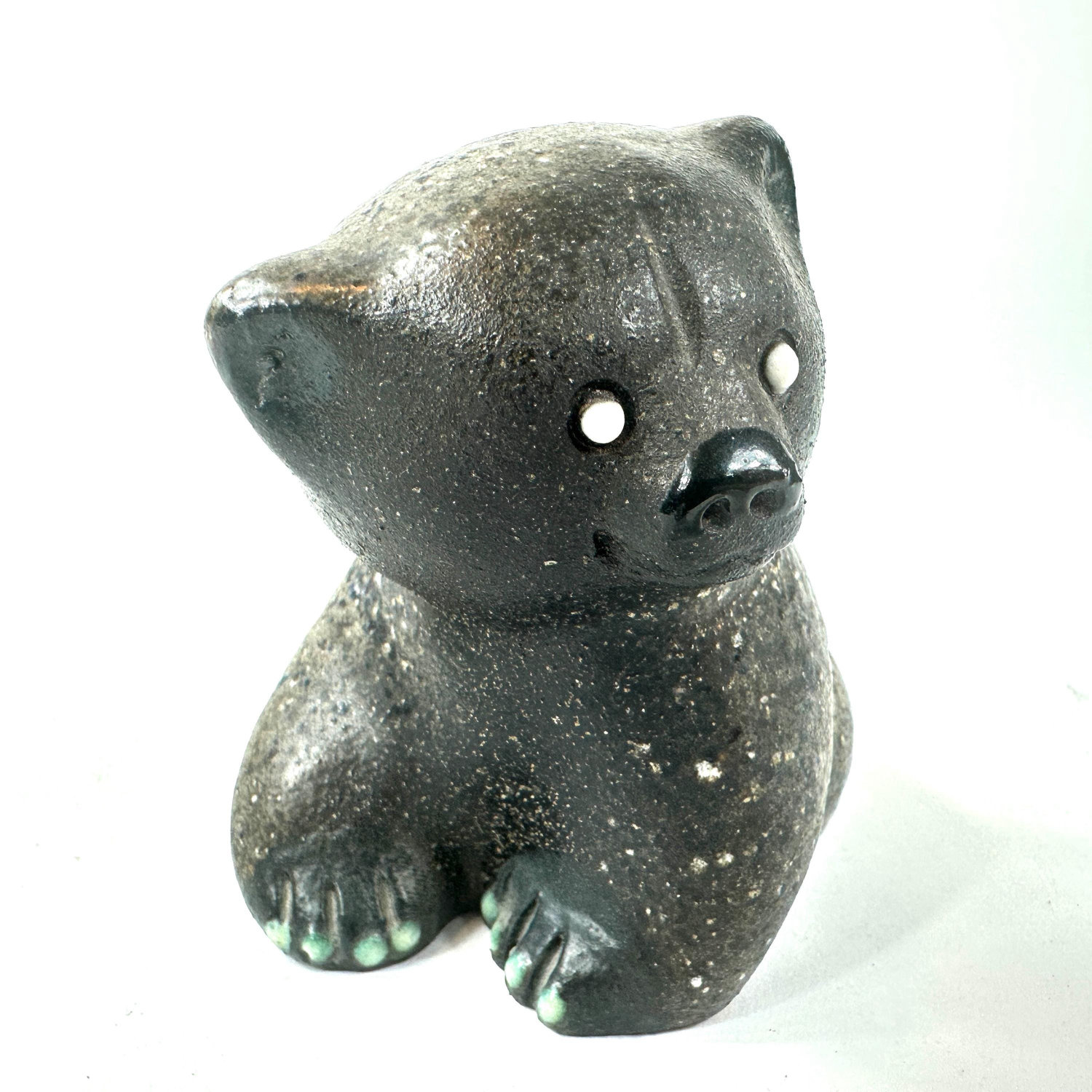 Small ceramic bear in left profile, green-tinted paws clearly visible, white eye detail, speckled gray stoneware texture thro