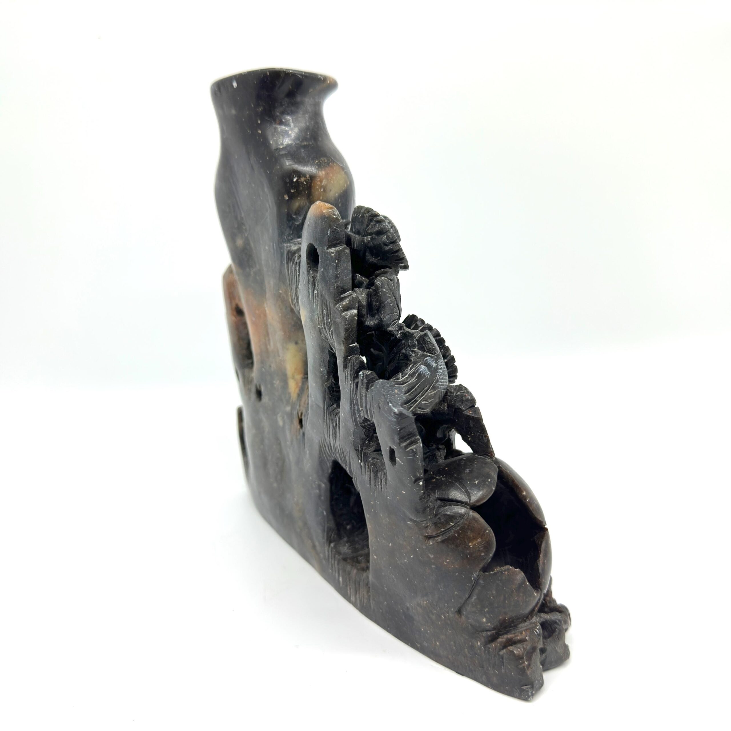 Soapstone sculpture tilted view showing carved bird silhouette, hollow aperture, and aged patina on dark stone