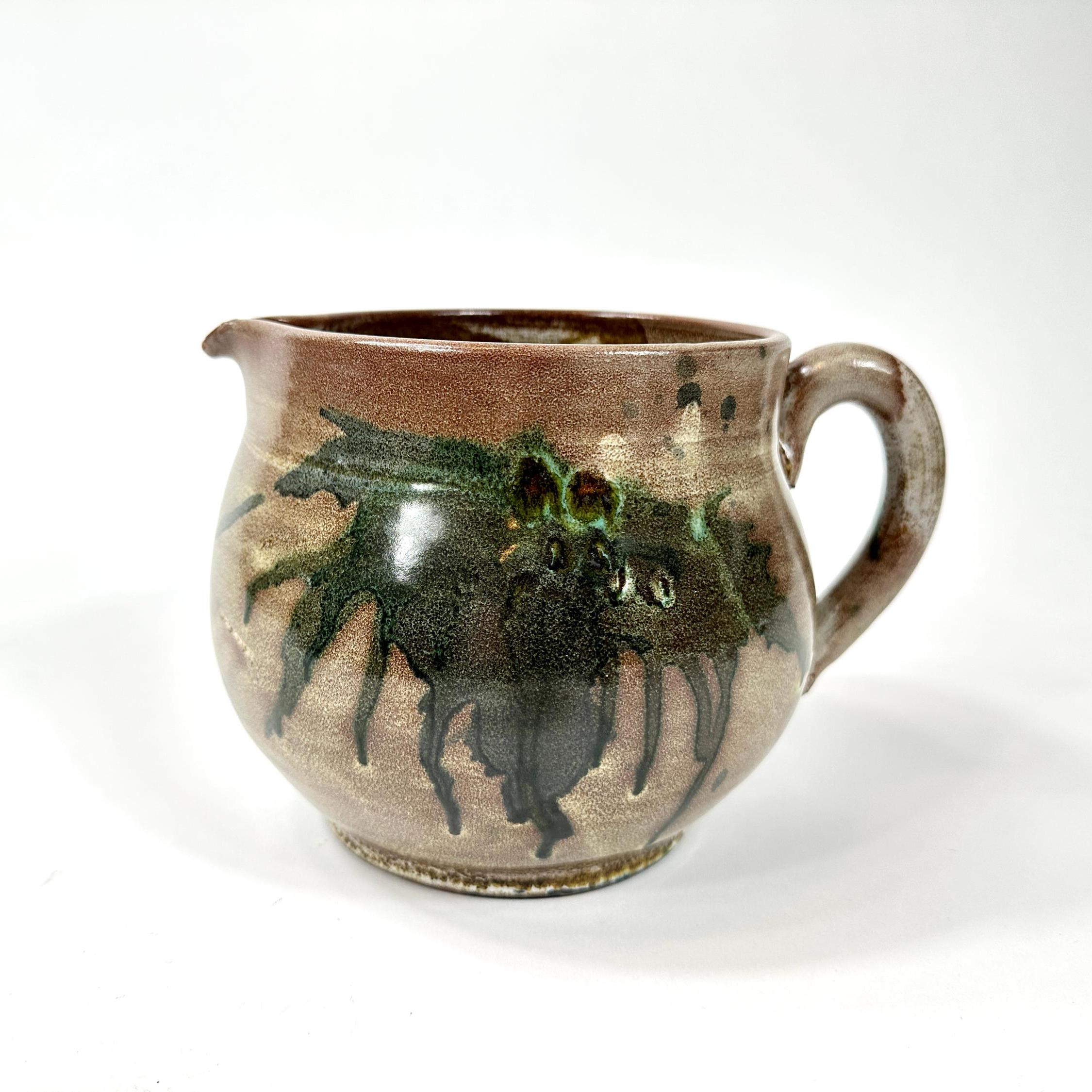 Stoneware pitcher showing profile with dramatic drip glaze cascading from rim down rounded body