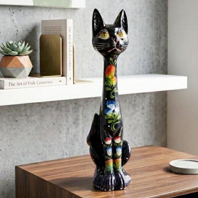 Tall black ceramic cat figurine with hand-painted yellow flowers and green eyes, displayed on wooden shelf with modern decor