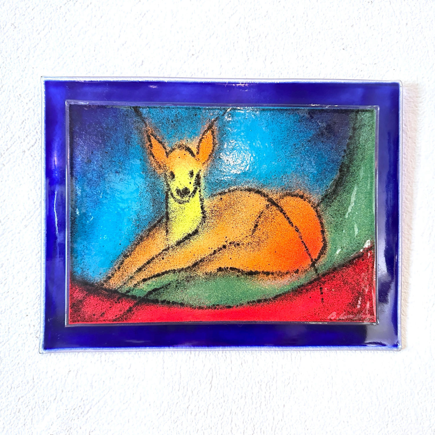Tilted wall view of framed glass art showing orange deer body and textured glass surface with emerald and sapphire color tran