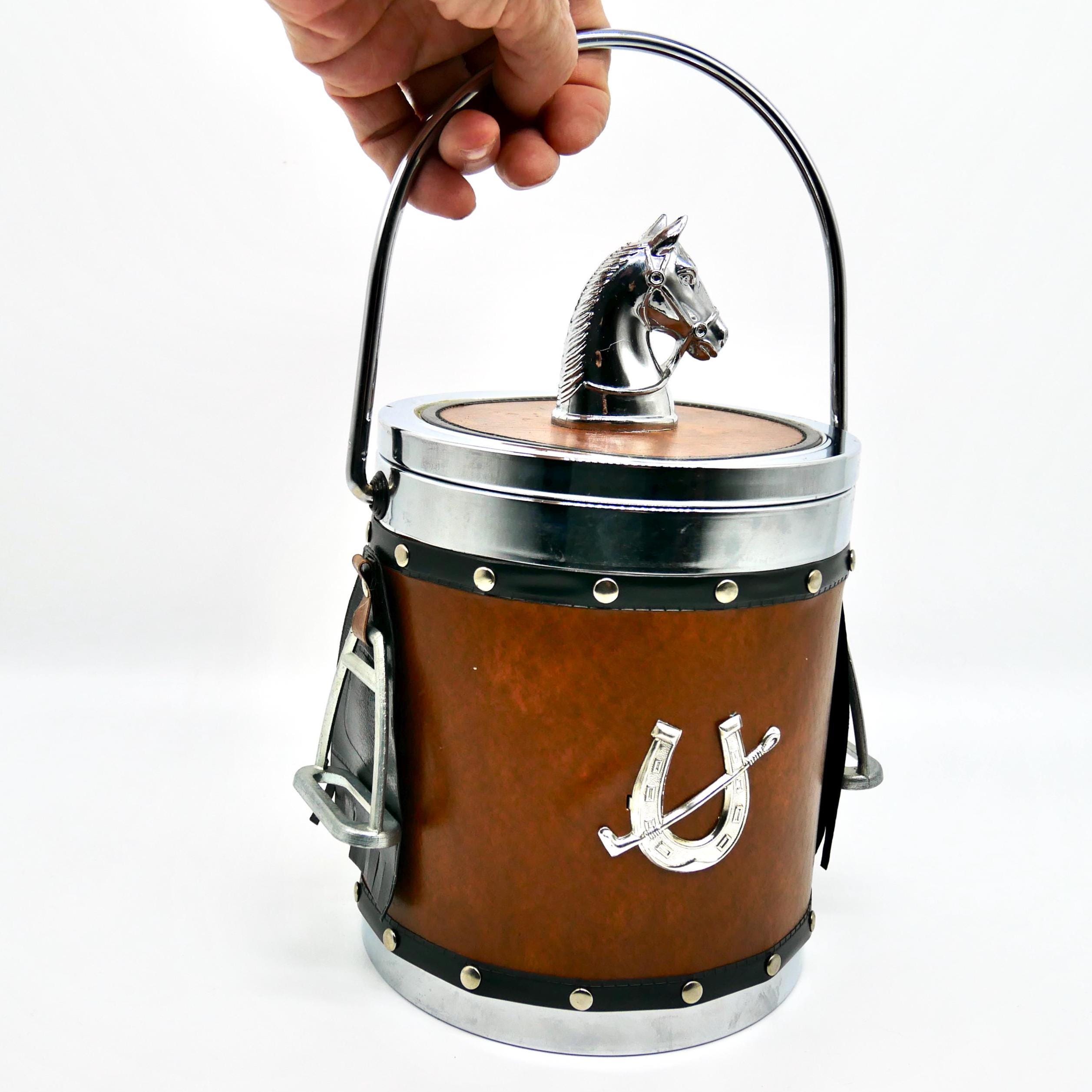 Vintage 1970s equestrian ice bucket with chrome horse head lid, faux leather body, and stirrup handles held in hand