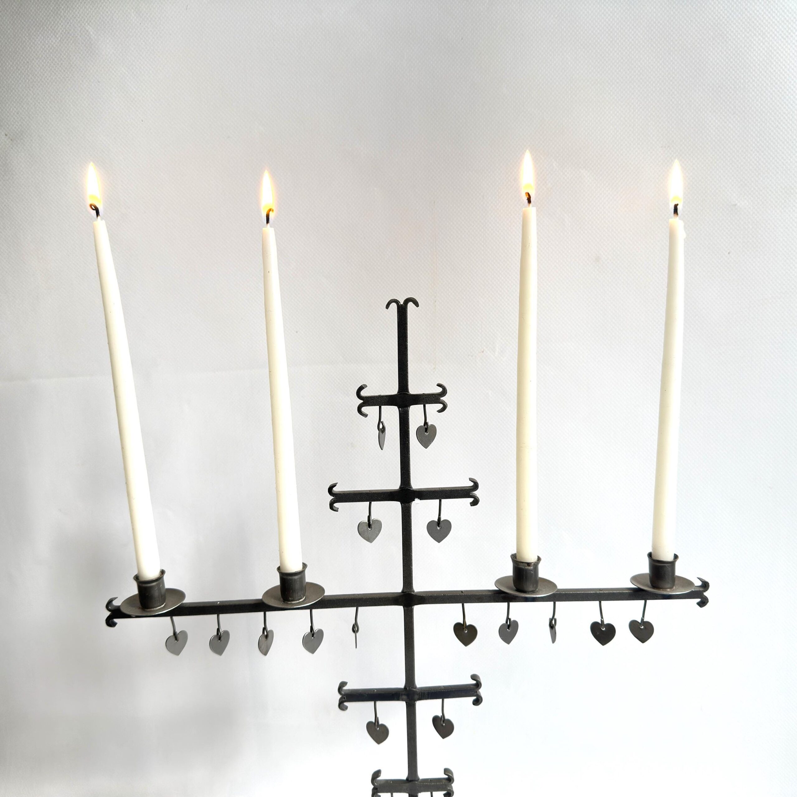 Wrought iron candelabra with four candles showing heart pendant details along horizontal and vertical iron arms, angled persp
