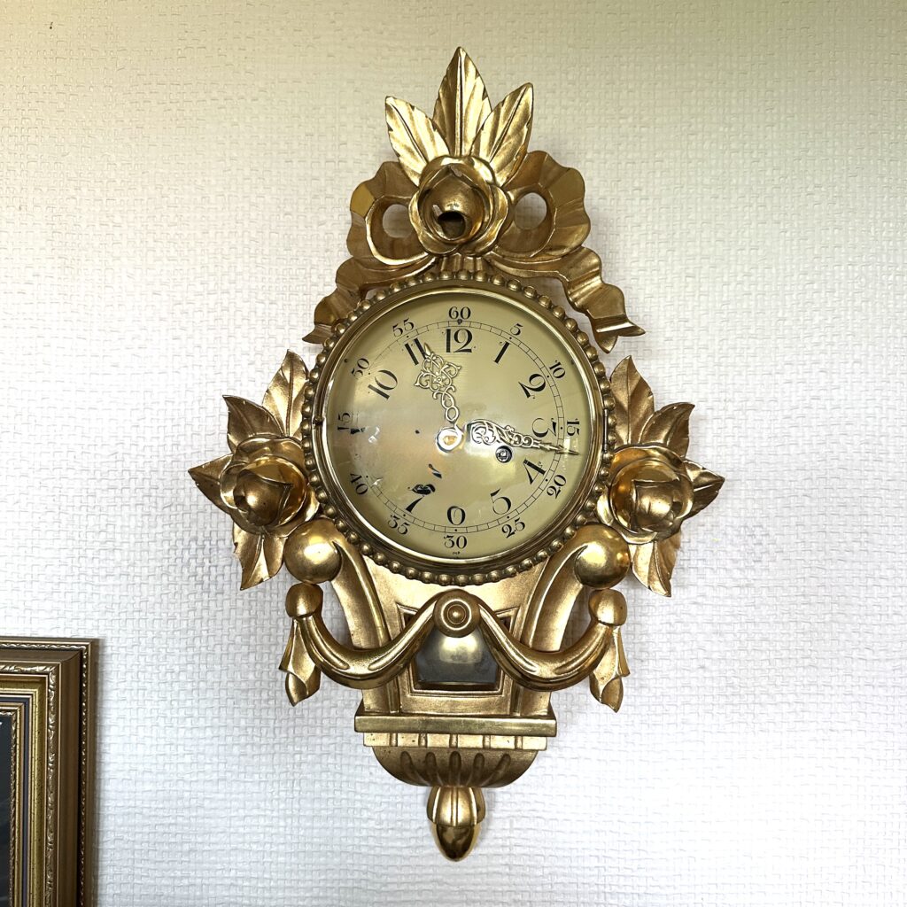 Ornate brass wall clock with scrollwork design, decorative crown finial, and aged gold patina