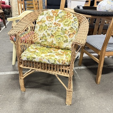 Woven wicker armchair with cheerful floral fabric cushions in botanical print, mid-century Scandinavian design piece ready fo