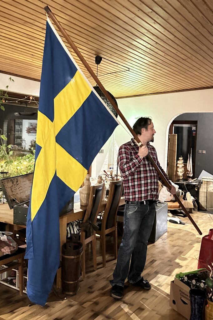 Large Swedish flag in navy and gold displayed indoors next to a figure, a commanding vintage textile spanning several feet in