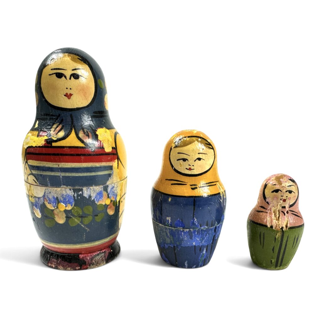 Three Russian matryoshka nesting dolls in graduated sizes with hand-painted details and visible wear from age