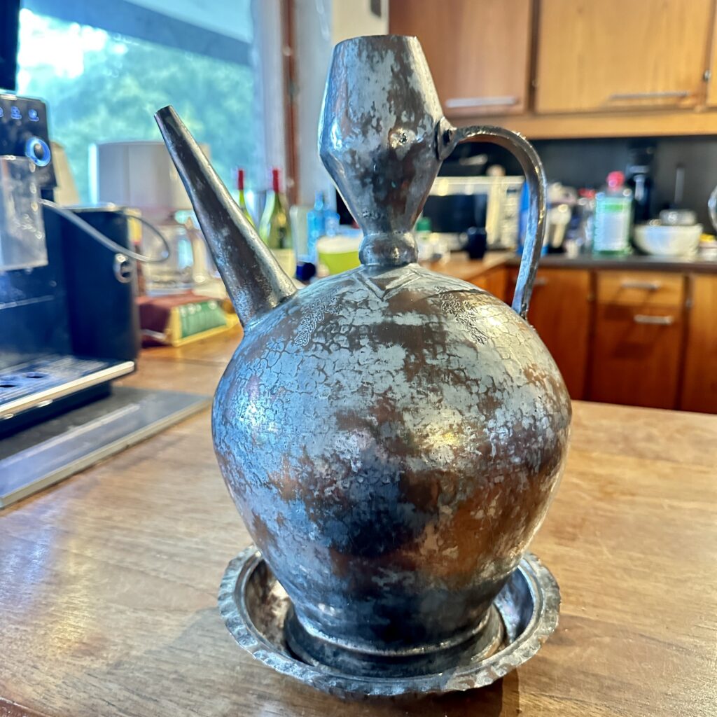 Antique copper ewer pitcher with patina and aged surface, rounded body form sitting on wooden table